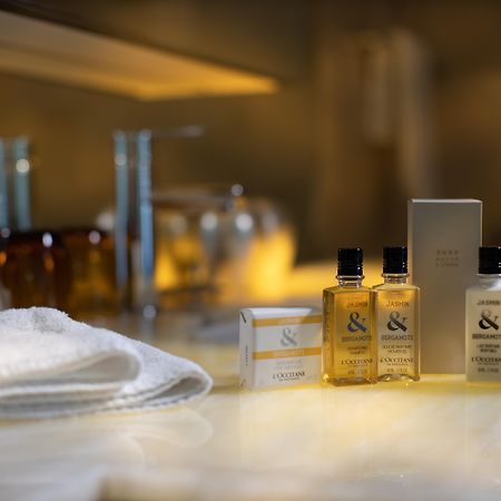 Traders Hotel, קואלה לומפור מראה חיצוני תמונה The photo shows a collection of personal care products arranged on a countertop. There are several small bottles of liquid, likely shampoo or body wash, with a couple of larger bottles and a box nearby. A soft white towel is also visible in the foreg
