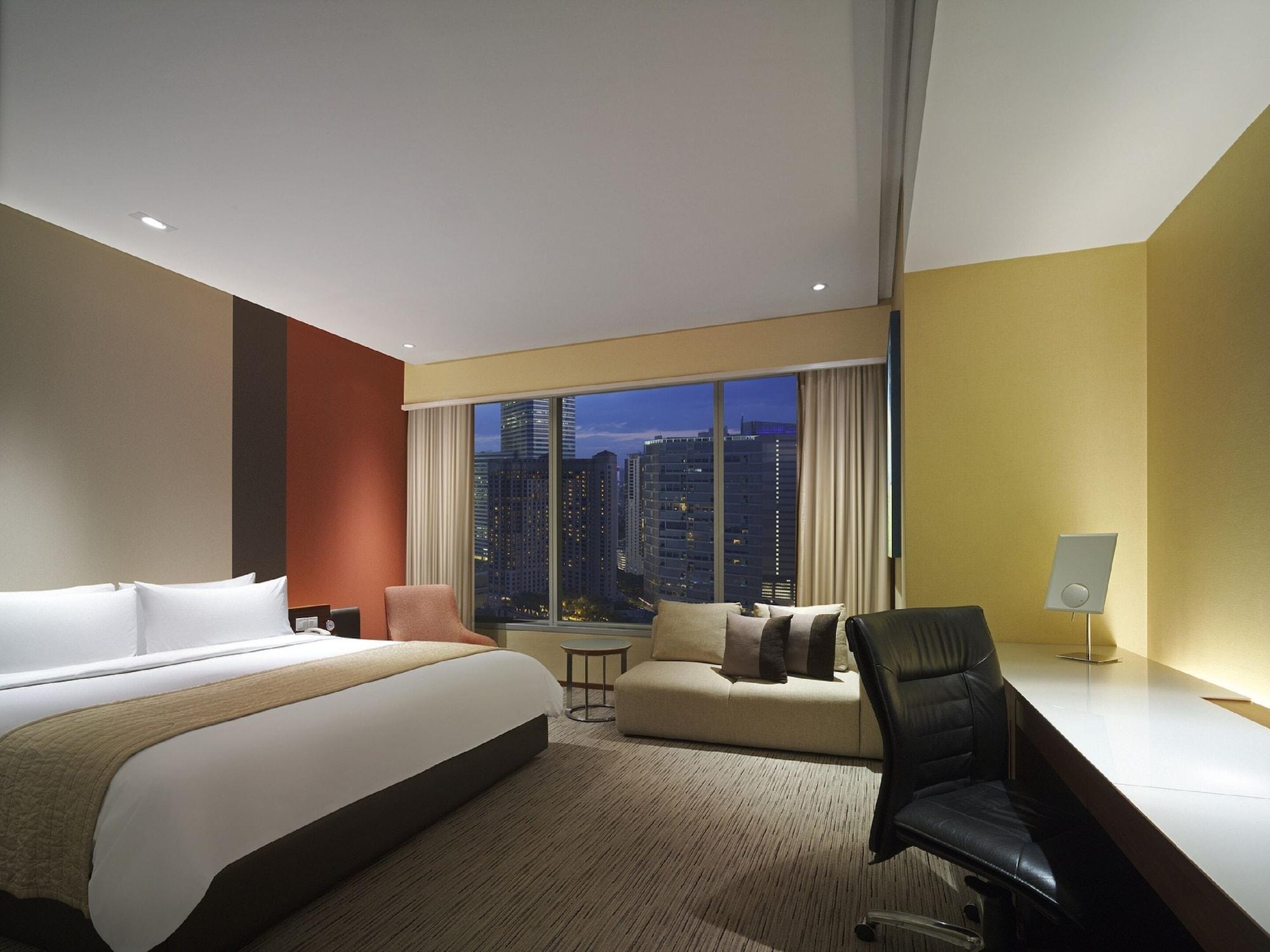 Traders Hotel, קואלה לומפור מראה חיצוני תמונה The photo shows a modern hotel room with a contemporary design. It features a large bed with white linens, positioned against a colorful wall. To the side of the bed, there is a cozy seating area with a sofa and a small table. A large window offers a