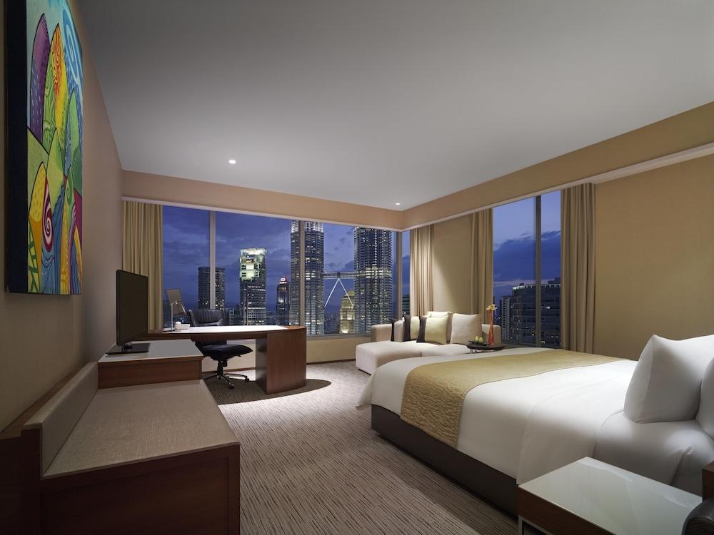 Traders Hotel, קואלה לומפור מראה חיצוני תמונה The photo shows a modern hotel room with large windows offering a view of a city skyline at dusk. The room features two beds, a desk with a chair, and a television. There is a decorative piece of artwork on the wall, adding a splash of color. The ove