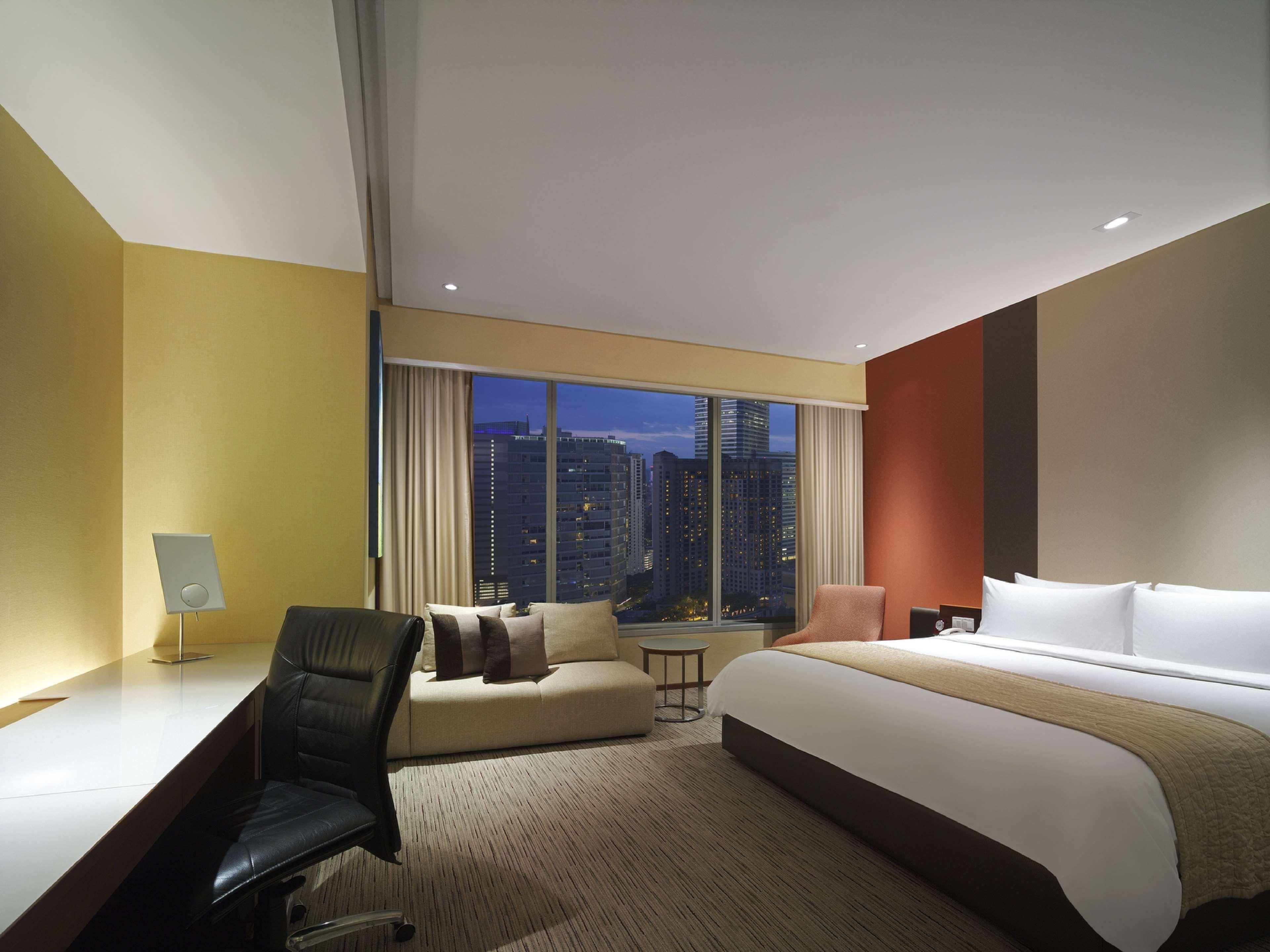 Traders Hotel, קואלה לומפור מראה חיצוני תמונה The photo depicts a modern hotel room featuring a large bed with white bedding and a brown accent. There is a cozy seating area with a chair and a sofa, along with a small coffee table. A desk is present, accompanied by an office chair, creating a fu