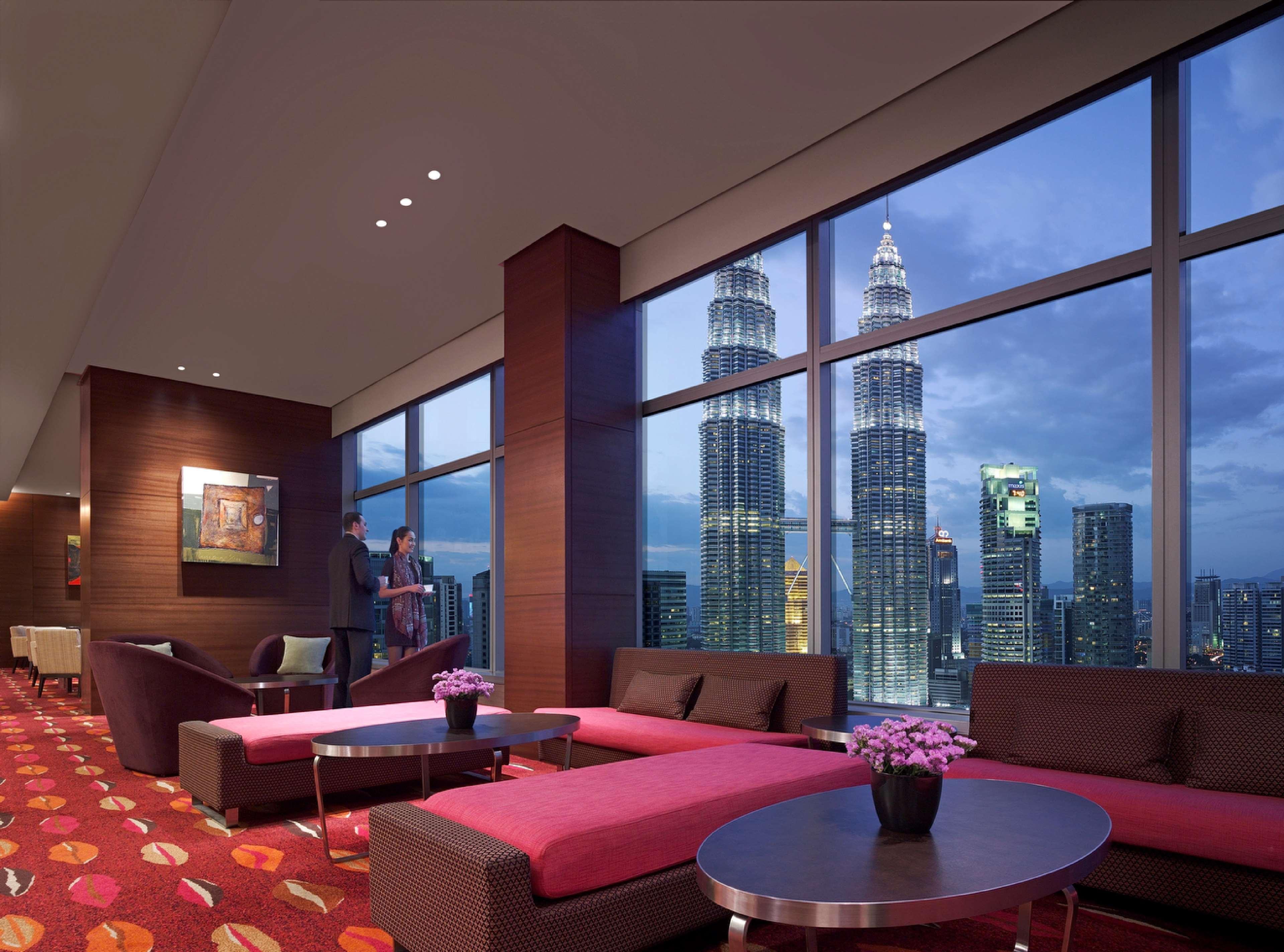 Traders Hotel, קואלה לומפור מראה חיצוני תמונה The photo shows a modern lounge or waiting area with large windows offering a view of tall skyscrapers, particularly the Petronas Towers, against a twilight sky. Inside, there are stylish, contemporary furnishings, including sofas and tables arranged