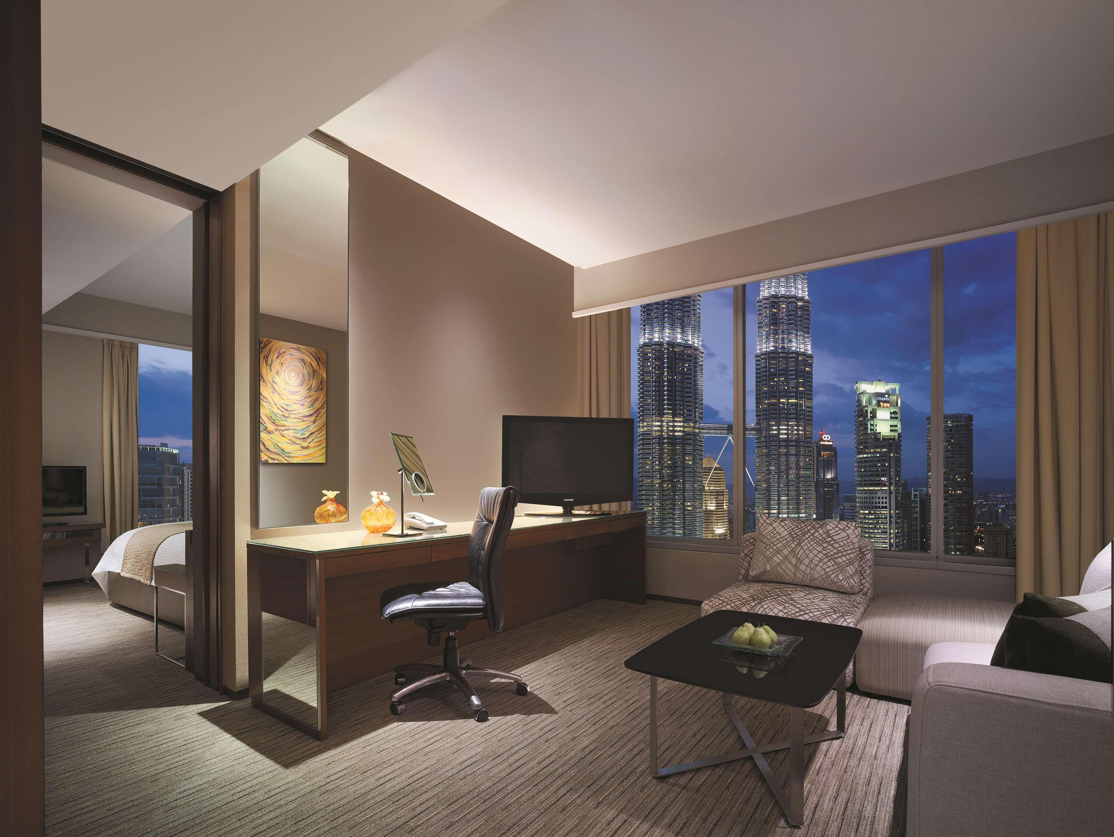 Traders Hotel, קואלה לומפור מראה חיצוני תמונה The photo shows a modern hotel room with an elegant design. The space features a cozy sitting area with a light-colored sofa and an armchair. A sleek desk with a chair is positioned nearby, along with a lamp and a flat-screen television mounted on th