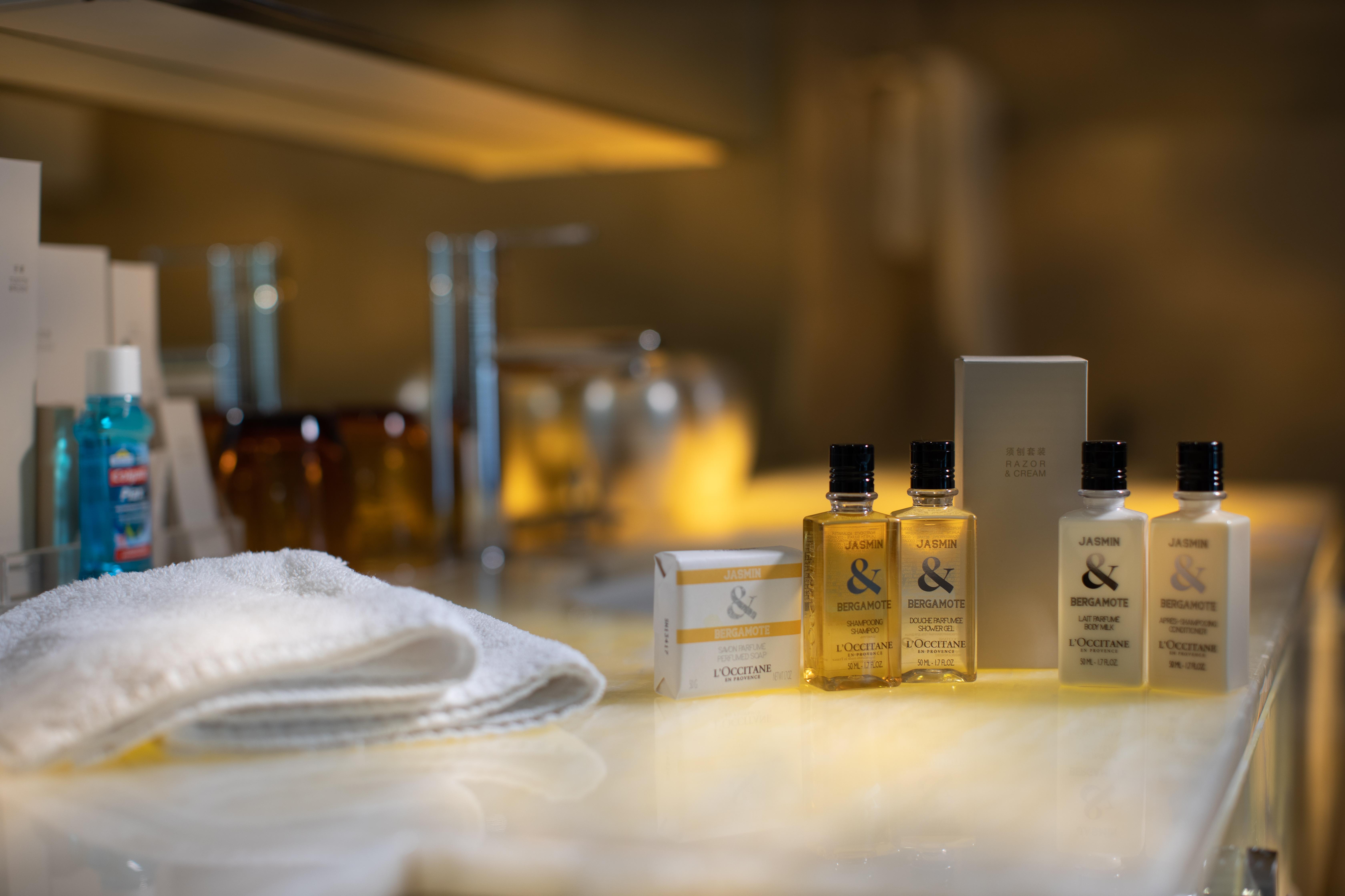 Traders Hotel, קואלה לומפור מראה חיצוני תמונה The photo shows a collection of personal care products arranged on a countertop. There are several small bottles of liquid, likely shampoo or body wash, with a couple of larger bottles and a box nearby. A soft white towel is also visible in the foreg