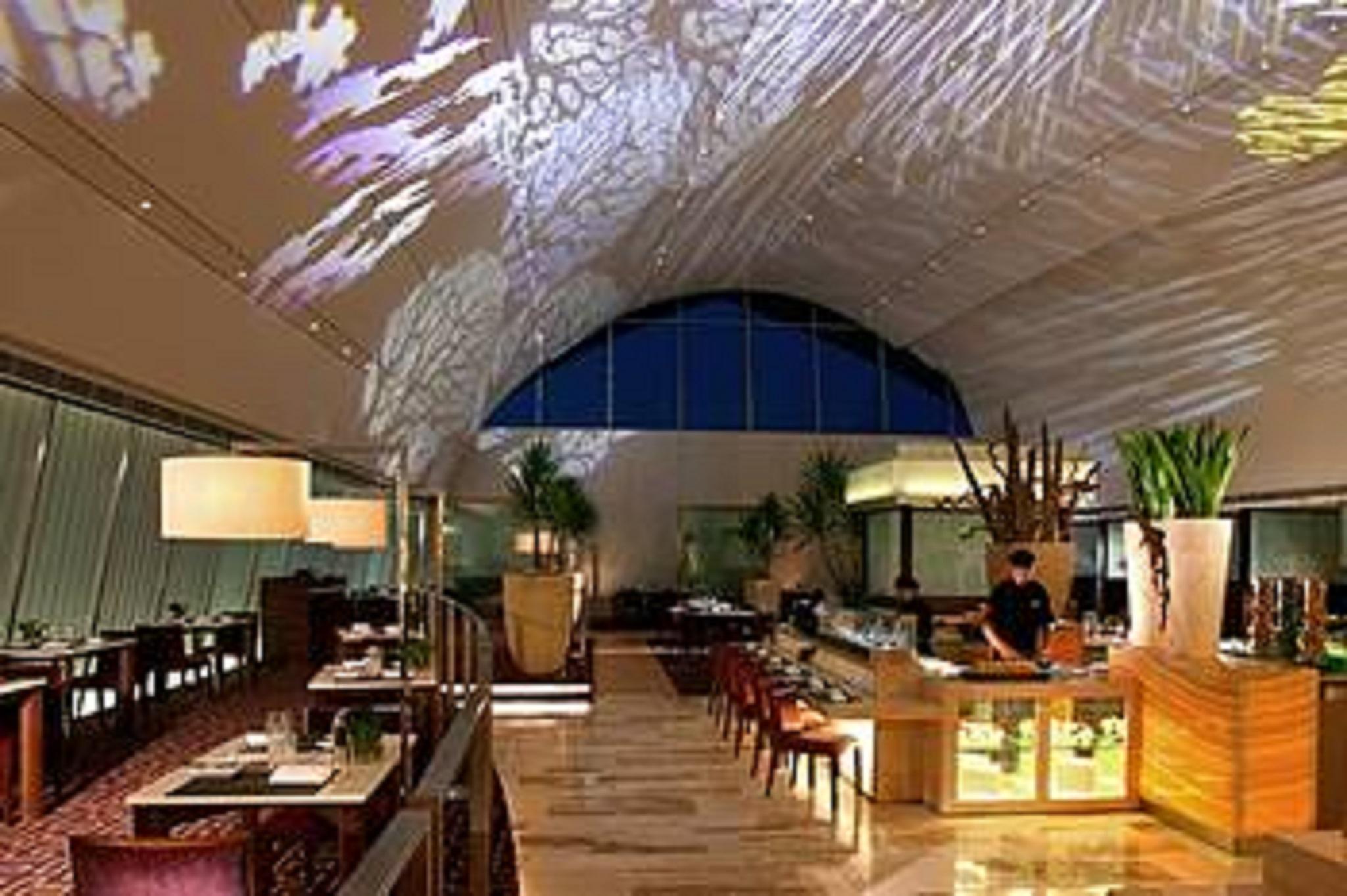 Traders Hotel, קואלה לומפור מראה חיצוני תמונה The photo shows the interior of a modern restaurant. The space features a high ceiling with a large arched window, allowing natural light to enter. A projection of intricate designs or patterns can be seen on the ceiling, adding a decorative touch. T