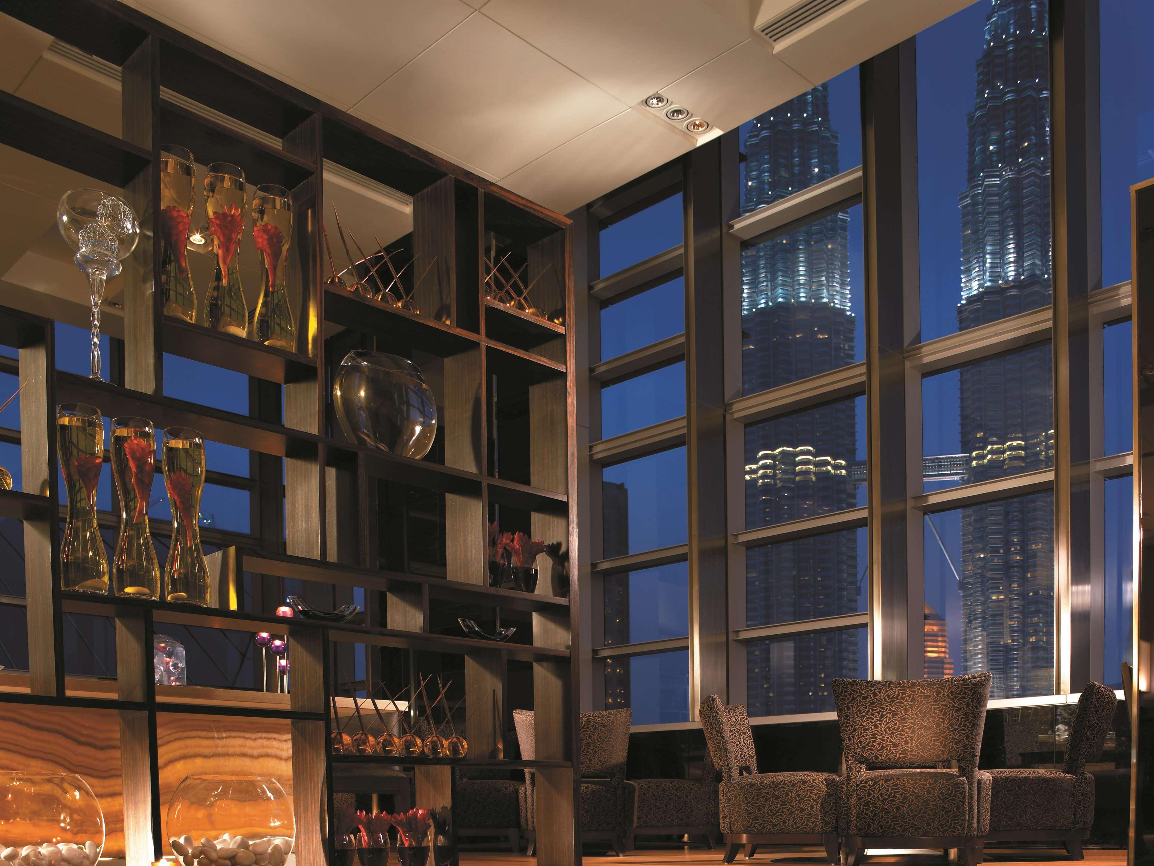 Traders Hotel, קואלה לומפור מראה חיצוני תמונה The photo shows a stylish and modern interior of a lounge or bar area. There is a prominent shelf with decorative glassware and elegant crystal items displayed, creating a sophisticated atmosphere. The setting features dark furnishings and several ch