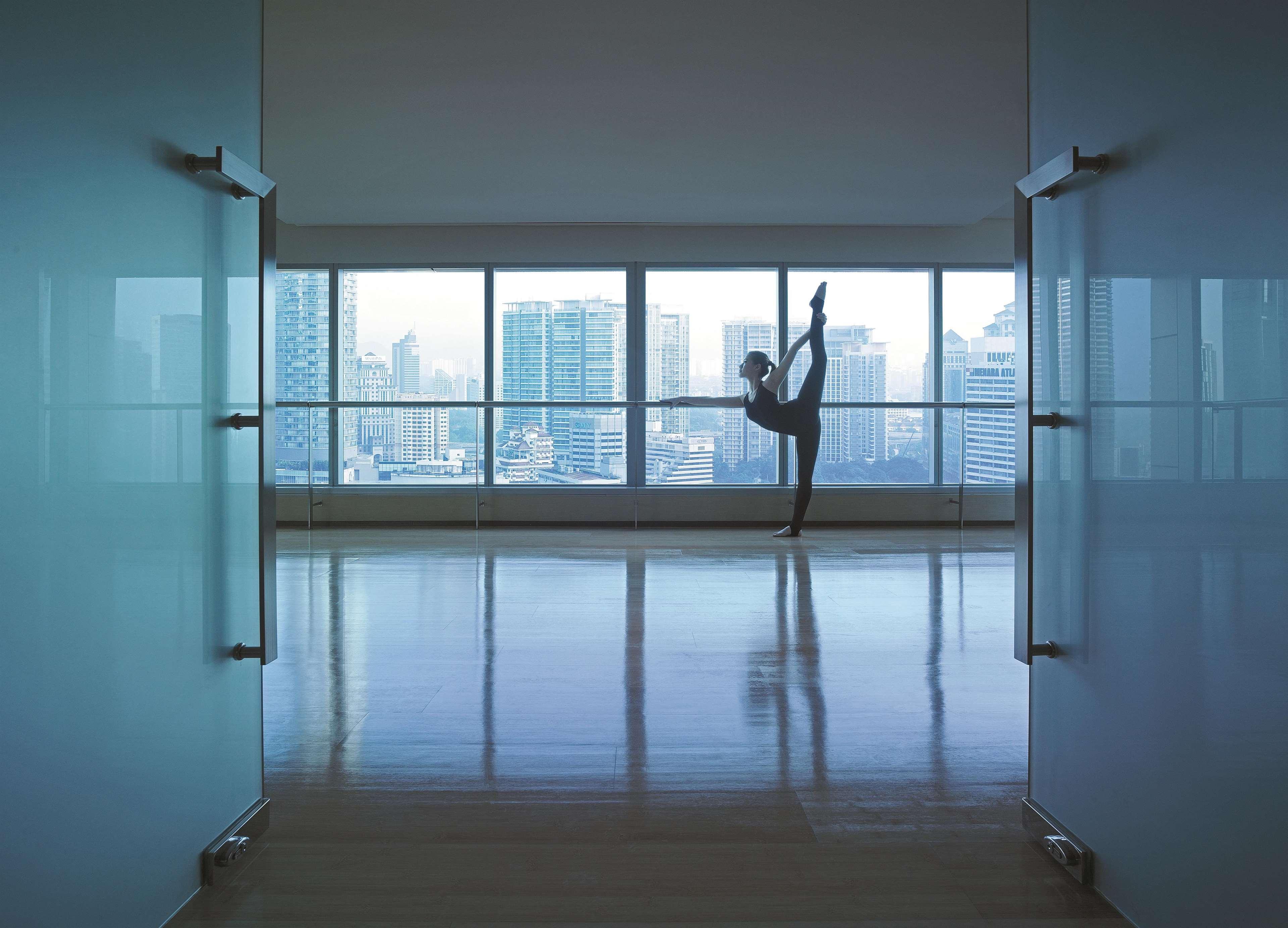 Traders Hotel, קואלה לומפור מראה חיצוני תמונה The photo shows a spacious, open studio with large glass windows that provide a view of a city skyline. Inside the studio, a dancer is captured in a striking pose, balancing on one leg with the other leg extended upward. The floor is shiny and reflec