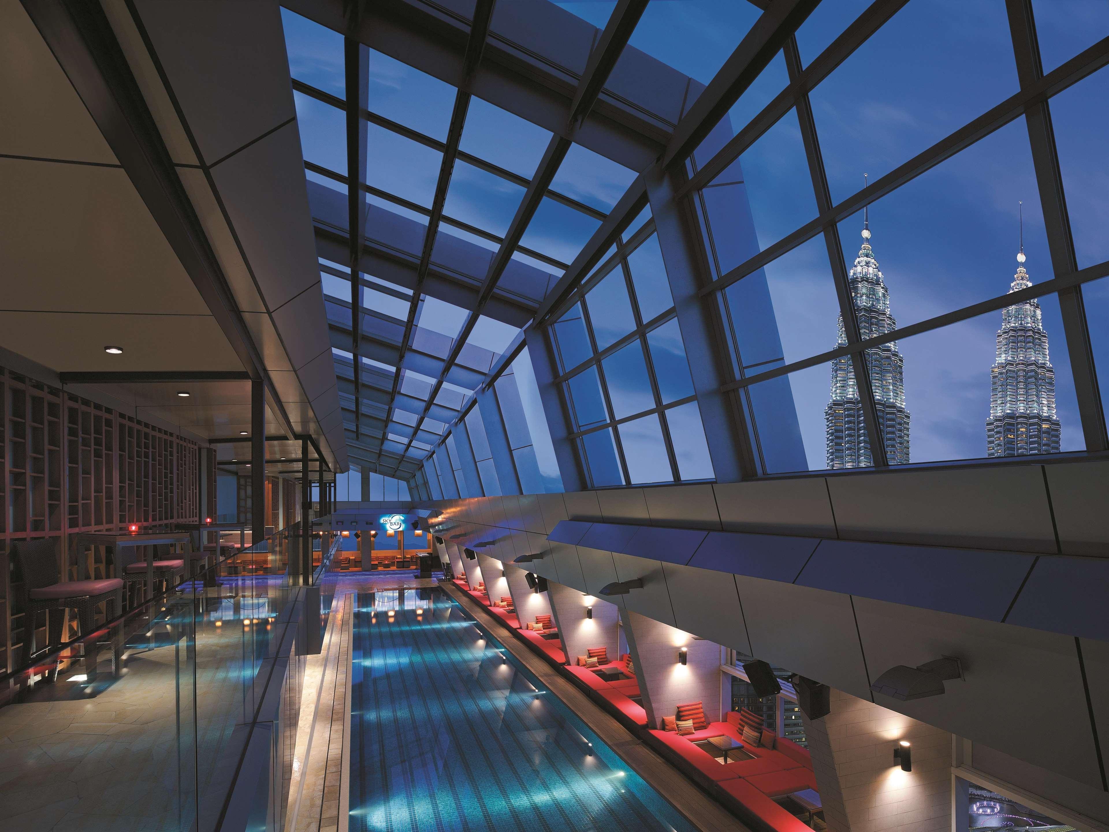 Traders Hotel, קואלה לומפור מראה חיצוני תמונה The photo shows an indoor swimming pool with a sleek, modern design. The pool is illuminated with blue lighting and is surrounded by large glass windows that allow for a view of the city outside. In the distance, two prominent skyscrapers, known as t