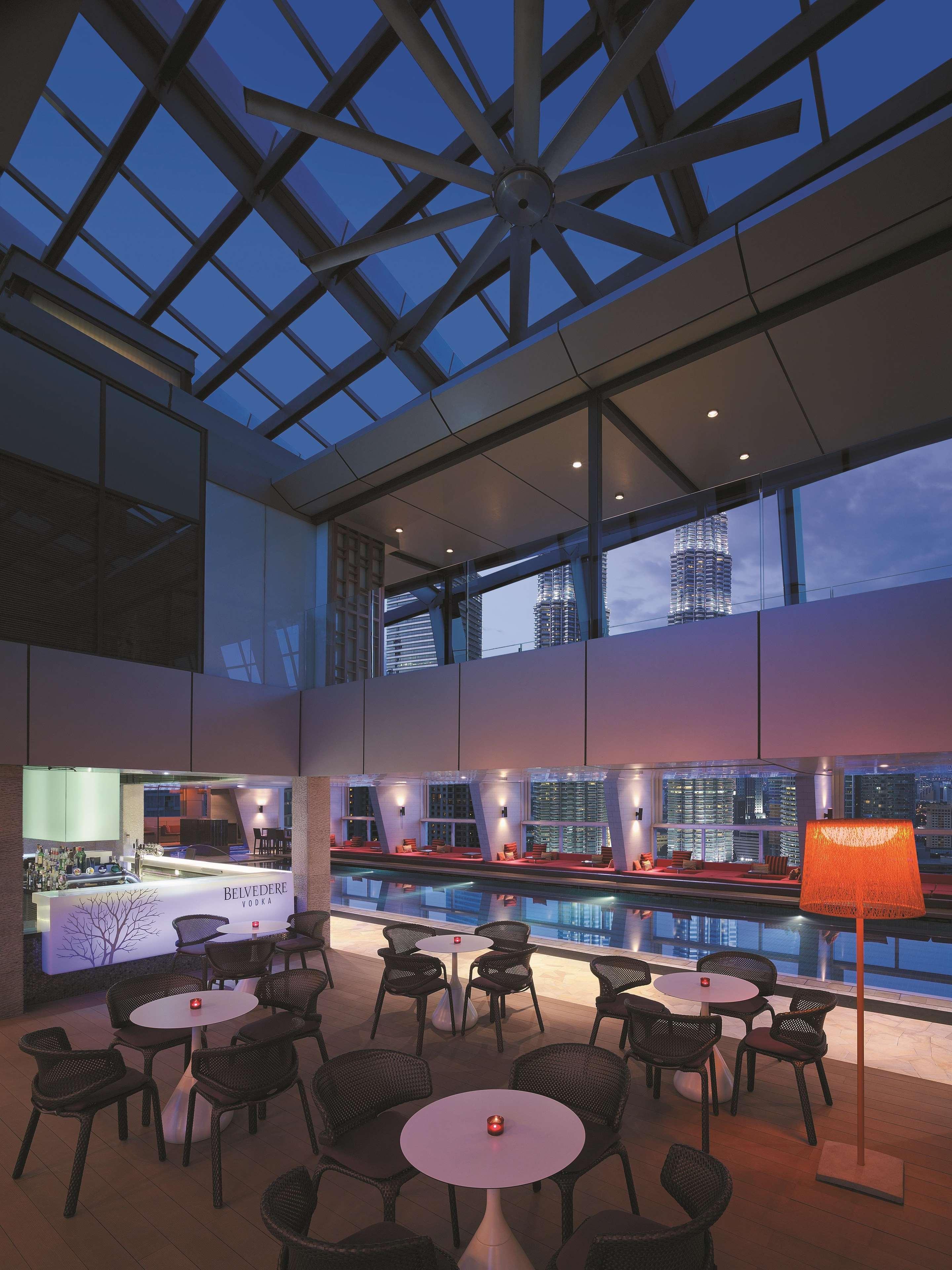 Traders Hotel, קואלה לומפור מראה חיצוני תמונה The photo showcases a stylish modern interior, featuring a spacious room with large glass windows that provide a stunning view of the skyline. The lighting is soft and ambient, creating a warm atmosphere as evening approaches. There are sleek furnitu
