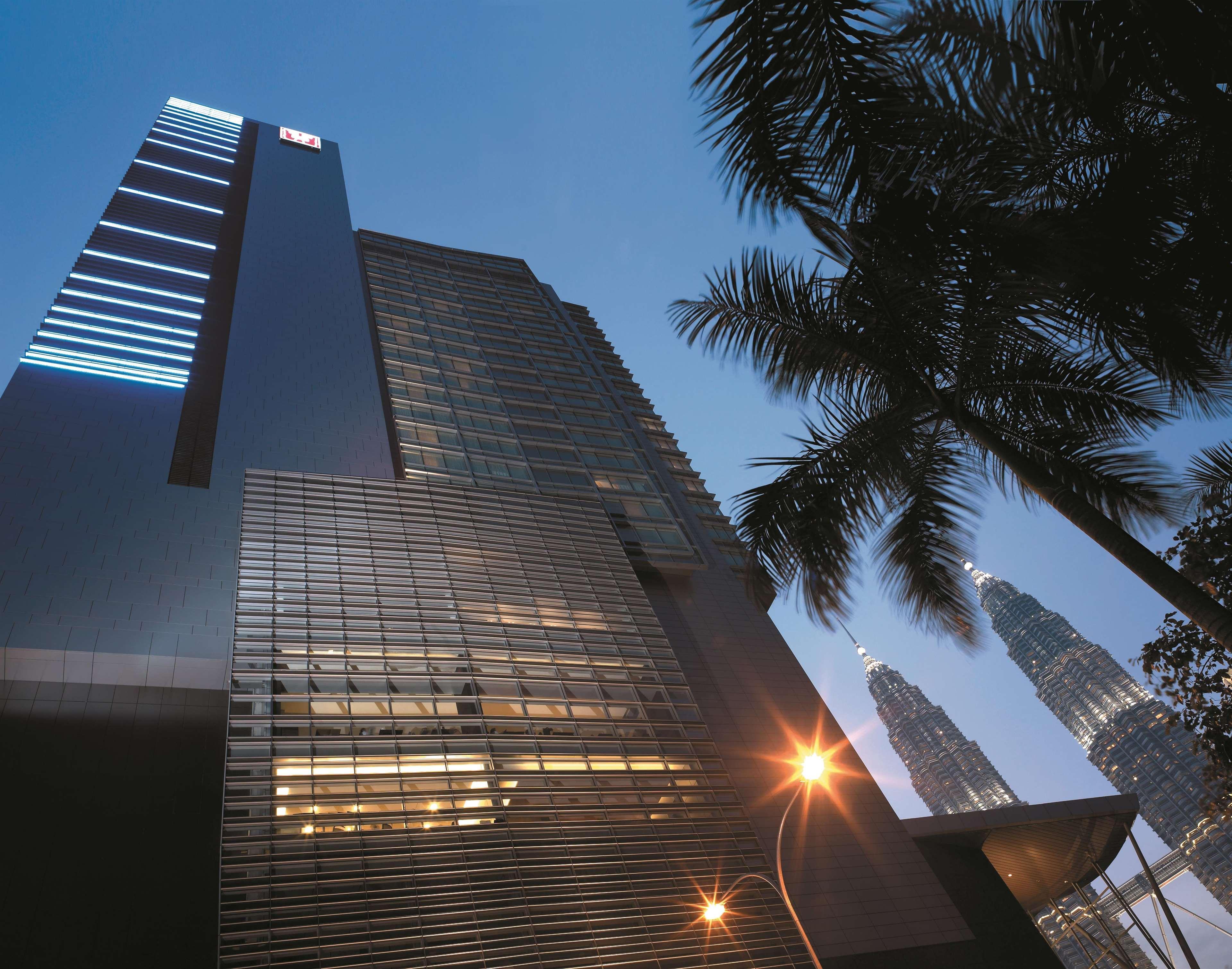 Traders Hotel, קואלה לומפור מראה חיצוני תמונה The photo shows a modern skyscraper partially illuminated in the evening light. The building features a sleek, glass facade with horizontal and vertical lines, showcasing a contemporary architectural style. In the background, there are iconic towers 