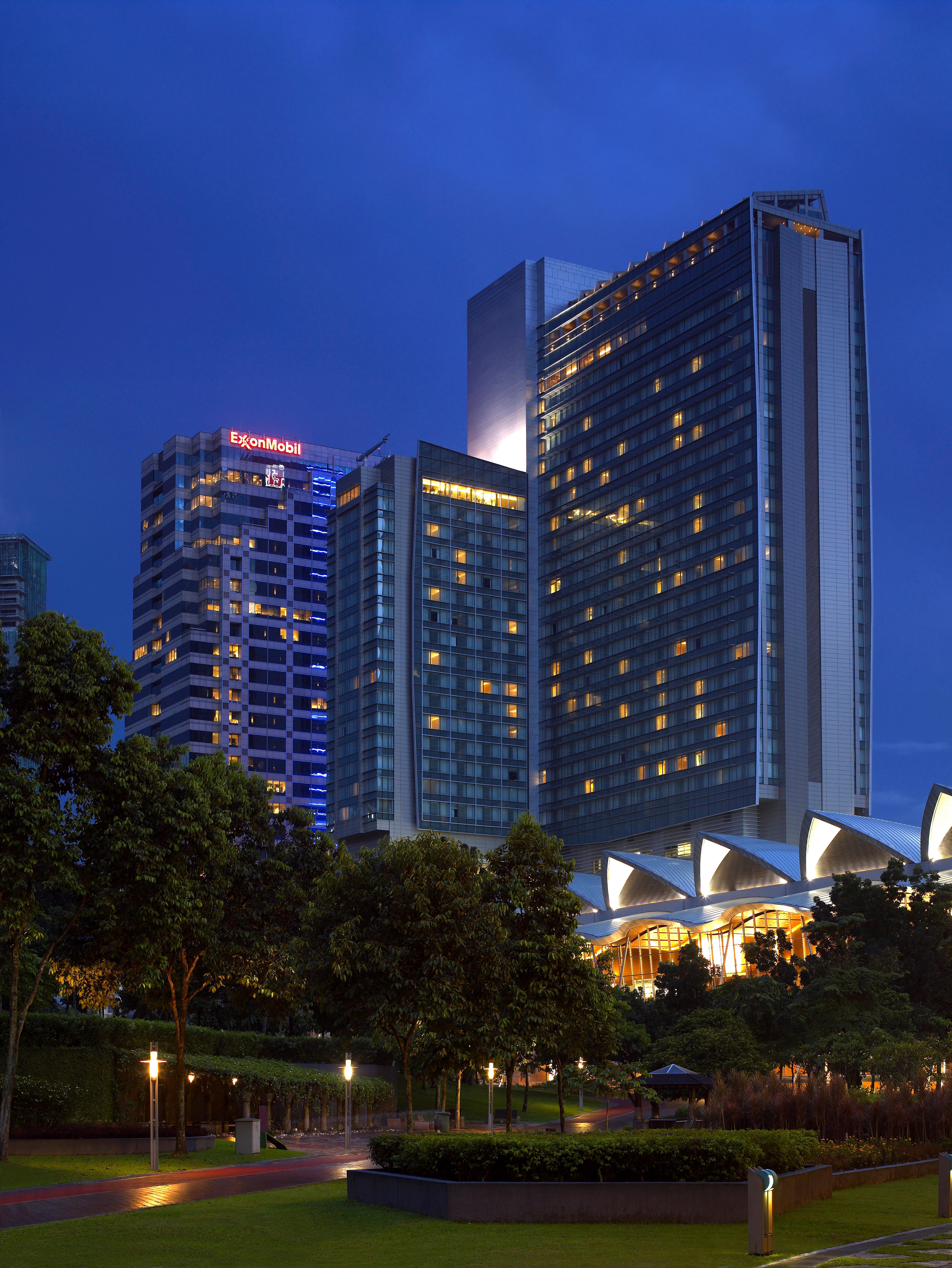 Traders Hotel, קואלה לומפור מראה חיצוני תמונה The photo shows a group of modern skyscrapers illuminated at dusk. The buildings feature glass facades, with varying designs and heights. Some of them have lights on, creating a vibrant atmosphere against the evening sky. In the foreground, there are
