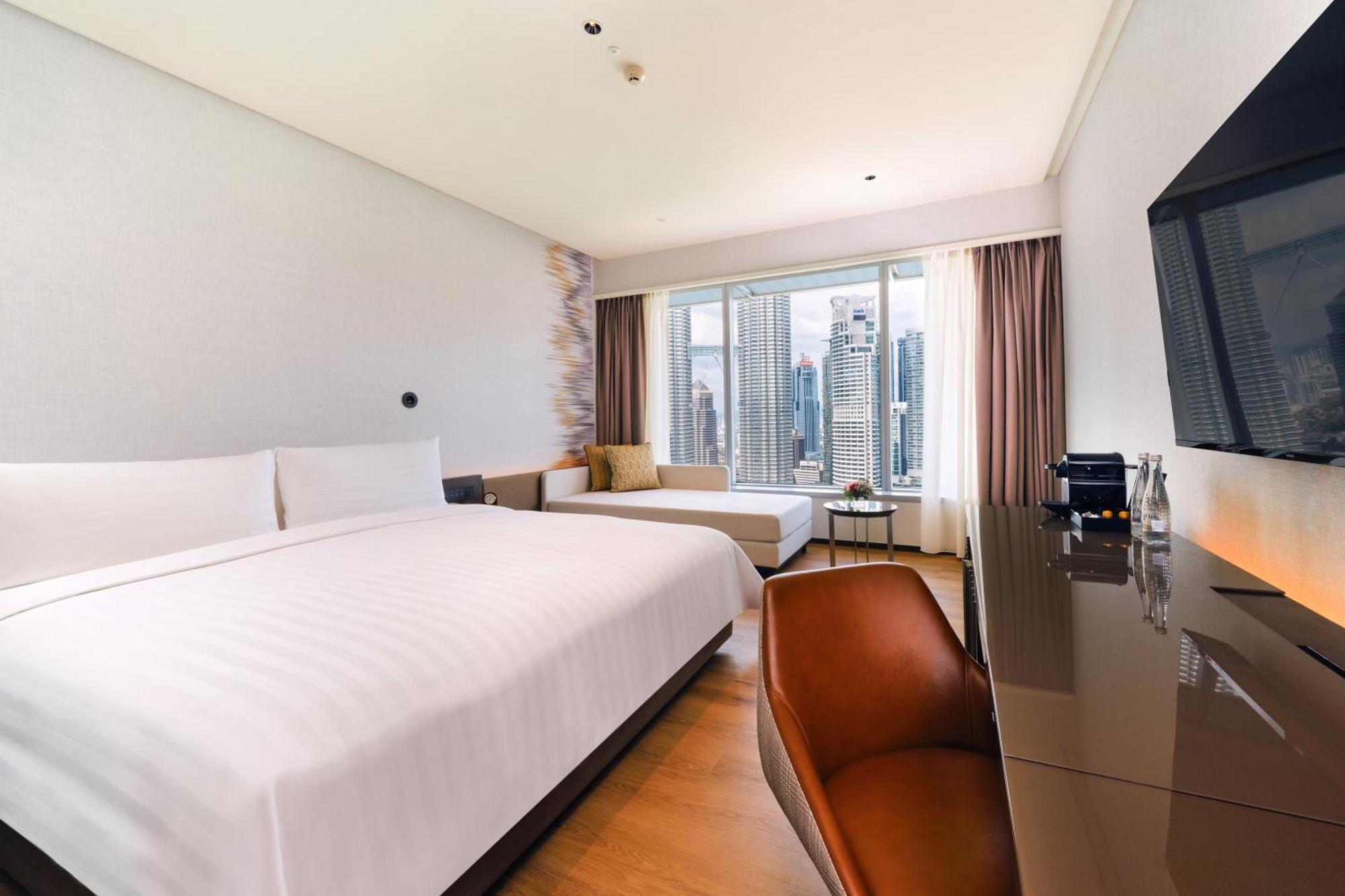 Traders Hotel, קואלה לומפור מראה חיצוני תמונה The photo shows a modern hotel room featuring two beds: a larger main bed and a smaller one adjacent to it. The room is well-lit and designed with a contemporary aesthetic, showcasing large windows that offer a view of a city skyline. There is a styl