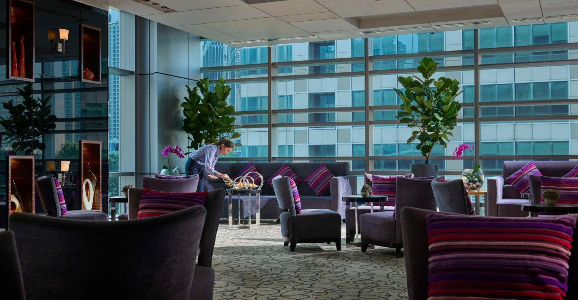 Traders Hotel, קואלה לומפור מראה חיצוני תמונה The photo shows a stylish and modern interior of a lounge or waiting area. It features plush seating arrangements with dark chairs and sofas, adorned with colorful striped cushions. Large plants and orchids add a touch of greenery to the space. There