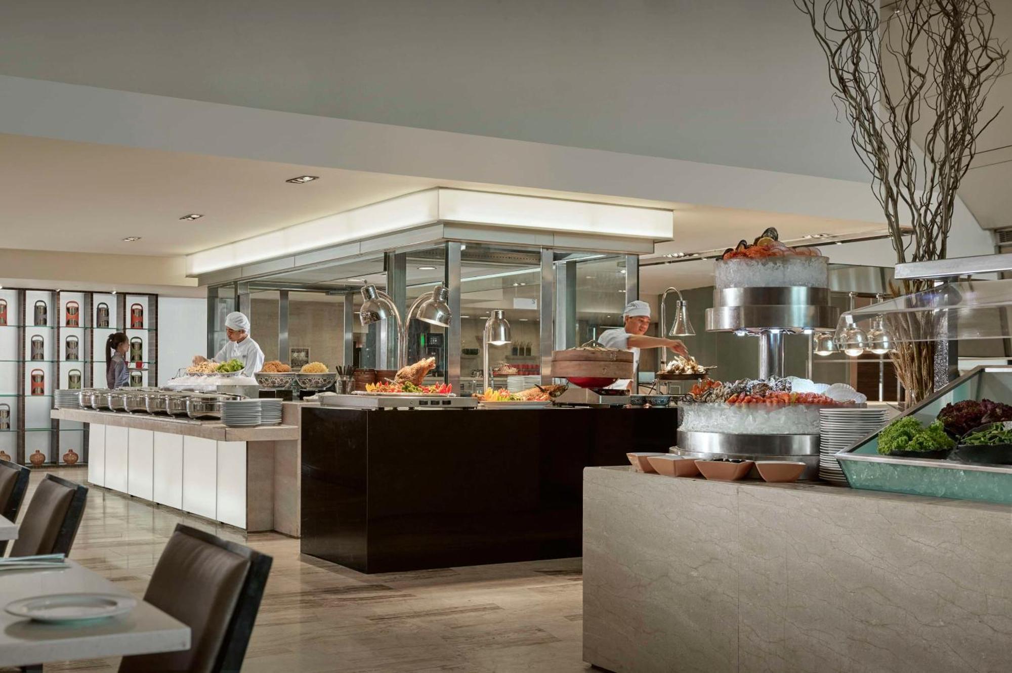 Traders Hotel, קואלה לומפור מראה חיצוני תמונה The photo shows a modern buffet-style restaurant or dining area. There is a large, well-organized food display featuring a variety of dishes, prominently positioned on a central serving counter. The food appears to be attractively arranged, with opti
