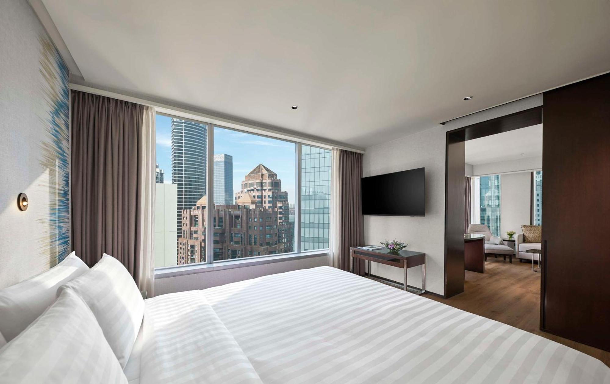 Traders Hotel, קואלה לומפור מראה חיצוני תמונה The photo shows a modern hotel room featuring a large bed with white linens. There is a large window that offers a view of the city skyline, showcasing tall buildings. The room is designed with a sleek, contemporary style, including warm wood accents