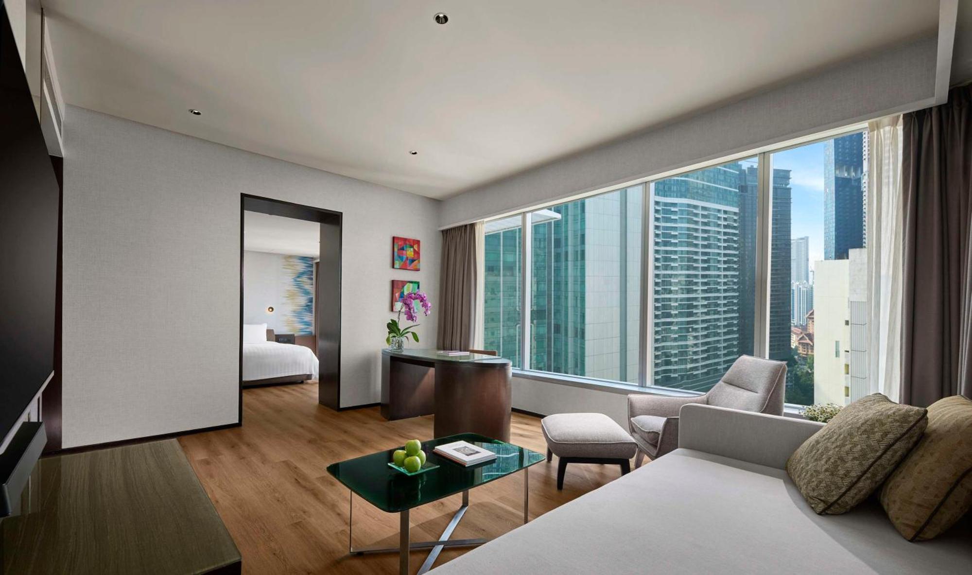 Traders Hotel, קואלה לומפור מראה חיצוני תמונה The photo shows a modern hotel room with a stylish design. There is a large window that provides a view of tall buildings outside, indicating a city setting. The room features a comfortable seating area with a chair and a small coffee table, which ha
