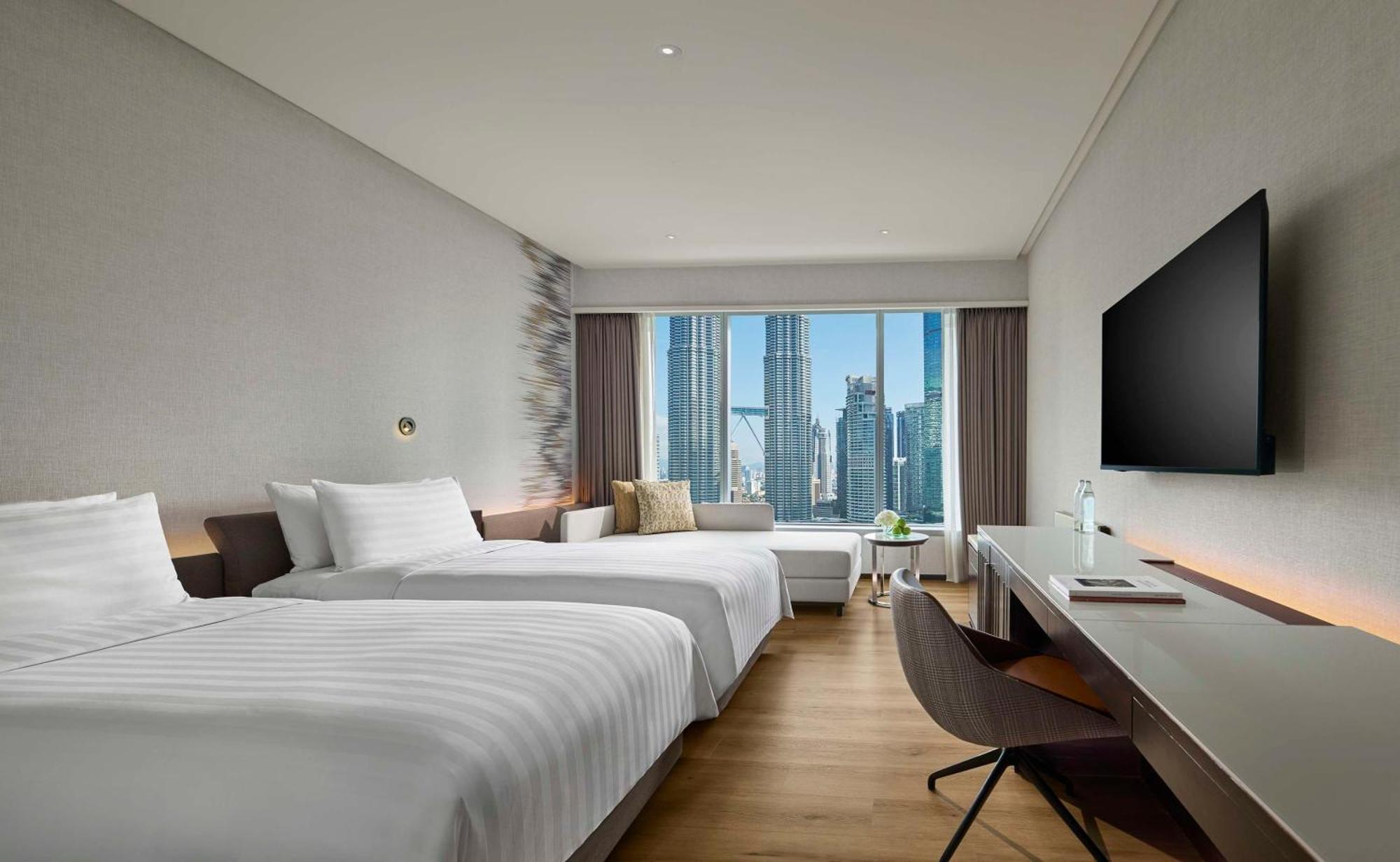 Traders Hotel, קואלה לומפור מראה חיצוני תמונה The photo shows a modern hotel room featuring two twin beds with white linens. The room has a minimalist design with light-colored walls and wooden flooring. Large windows provide a view of tall buildings outside, adding to the urban atmosphere. Ther