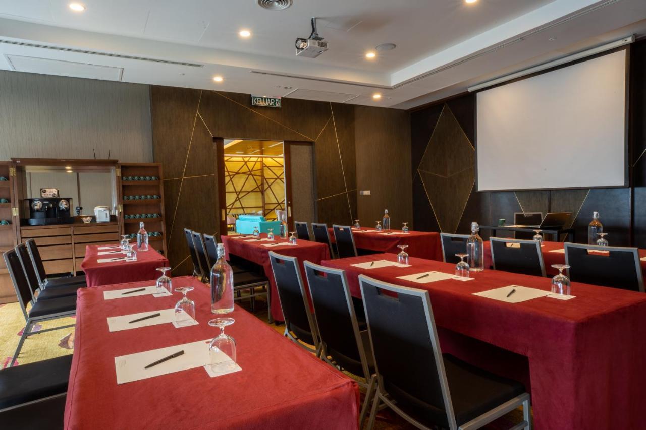 Traders Hotel, קואלה לומפור מראה חיצוני תמונה The photo shows a conference room set up for a meeting or seminar. There are several tables covered with red tablecloths, and each table is equipped with a notepad and pen. Transparent water glasses are placed on each table. The room has a modern des